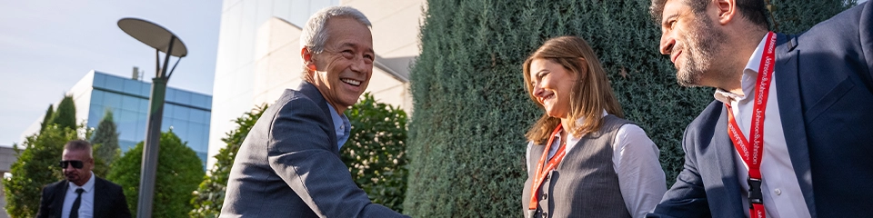 Joaquin Duato smiling and shaking hands with two people wearing J&J lanyards (photo)