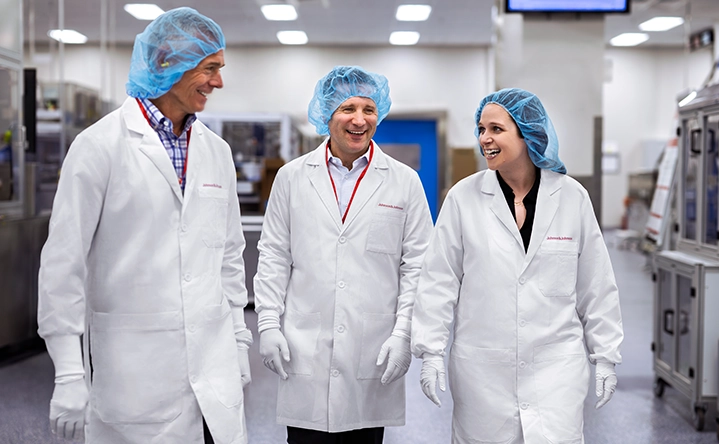 Three happy employees with lab coats, gloves and hair nets walking through a lab (photo)